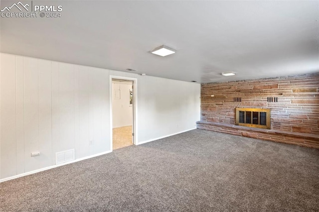 unfurnished living room with carpet floors, wooden walls, and a stone fireplace