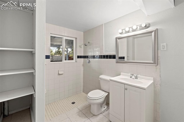 bathroom featuring a tile shower, vanity, tile walls, tile patterned flooring, and toilet