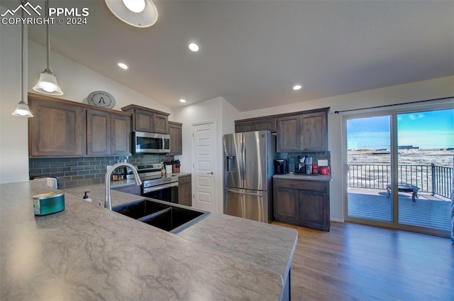 kitchen featuring pendant lighting, lofted ceiling, sink, decorative backsplash, and appliances with stainless steel finishes