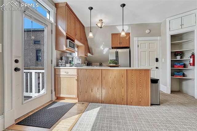 kitchen featuring stainless steel refrigerator, sink, pendant lighting, and light hardwood / wood-style floors