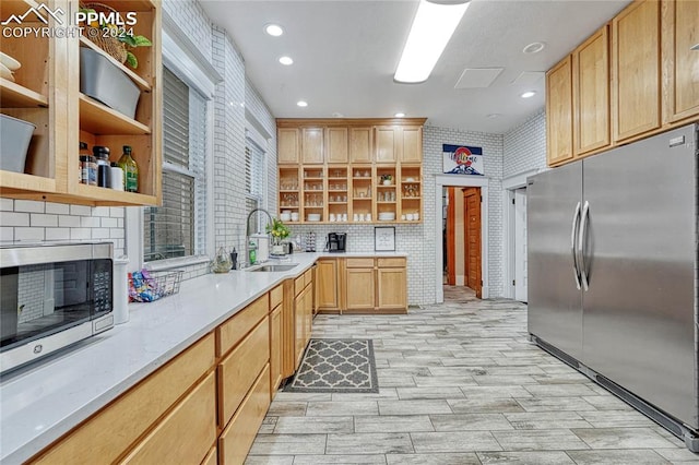 kitchen with appliances with stainless steel finishes, backsplash, light brown cabinetry, and sink