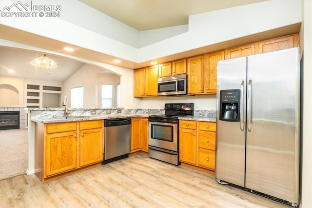 kitchen featuring stainless steel appliances, sink, a fireplace, light stone counters, and a chandelier