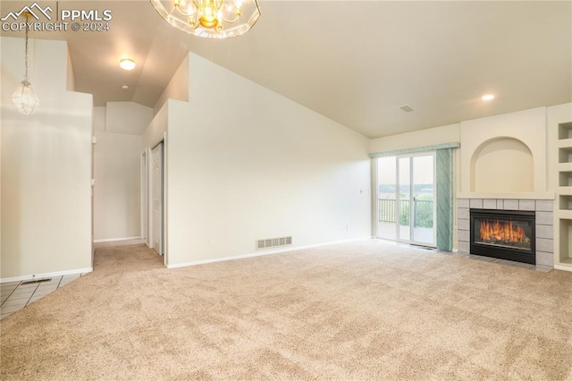 unfurnished living room with lofted ceiling, a tiled fireplace, an inviting chandelier, and carpet