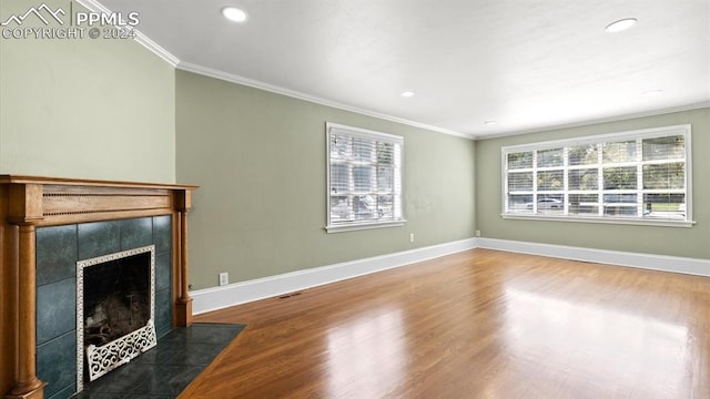 unfurnished living room featuring a tiled fireplace, hardwood / wood-style flooring, ornamental molding, and a healthy amount of sunlight