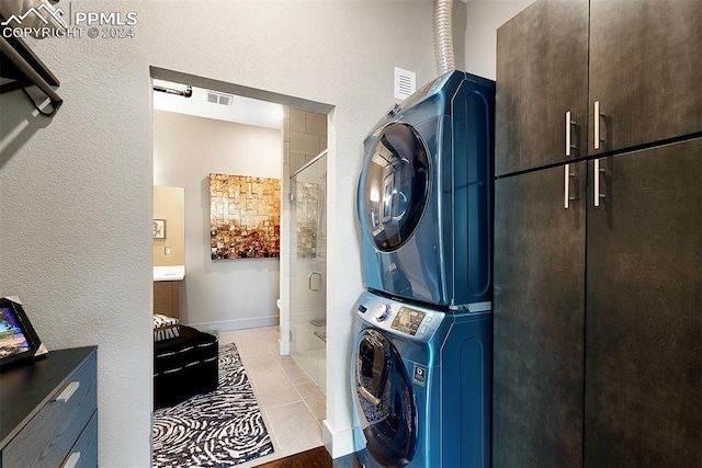 laundry room with cabinets, light tile patterned floors, and stacked washer and clothes dryer