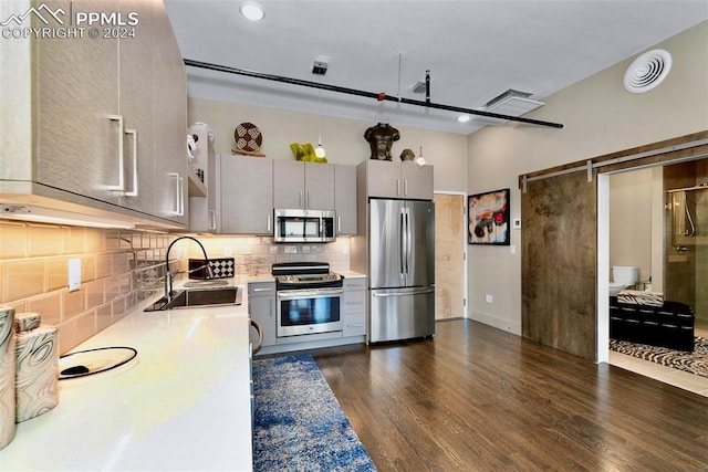 kitchen with decorative backsplash, appliances with stainless steel finishes, dark hardwood / wood-style flooring, sink, and a barn door