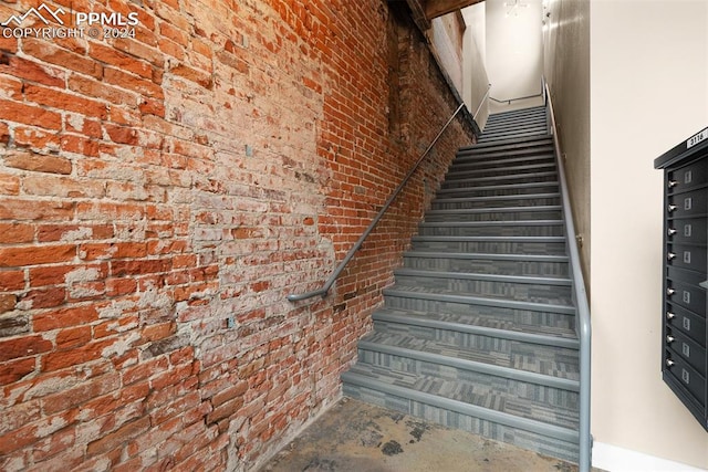 stairs featuring concrete flooring and brick wall