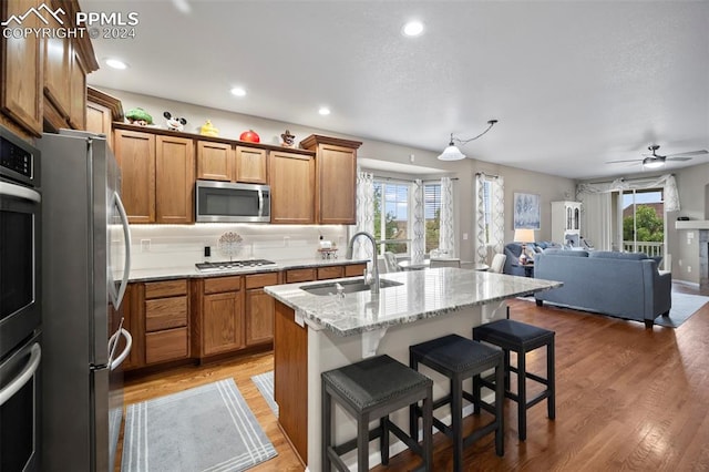 kitchen featuring stainless steel appliances, sink, a kitchen breakfast bar, ceiling fan, and a center island with sink