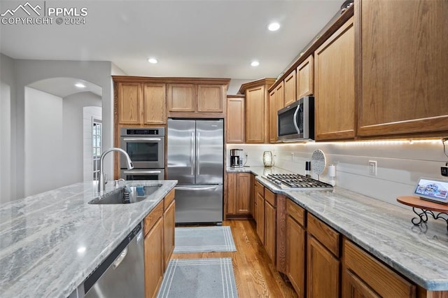 kitchen with light hardwood / wood-style flooring, backsplash, sink, light stone countertops, and appliances with stainless steel finishes