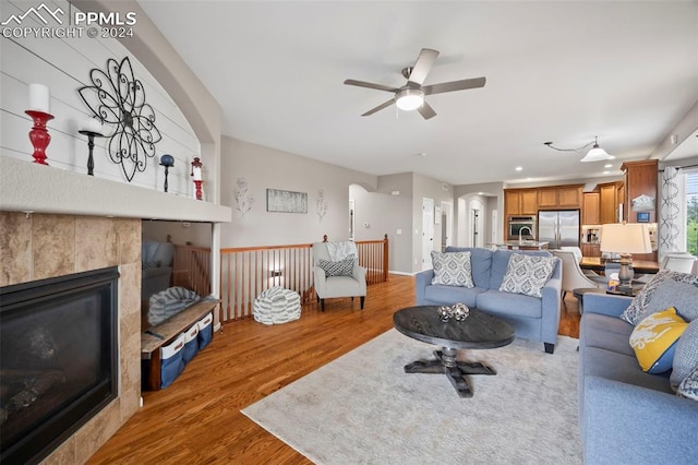 living room with wood-type flooring, a tile fireplace, and ceiling fan