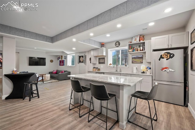 kitchen with light wood-type flooring, stainless steel fridge, a breakfast bar area, and white cabinets