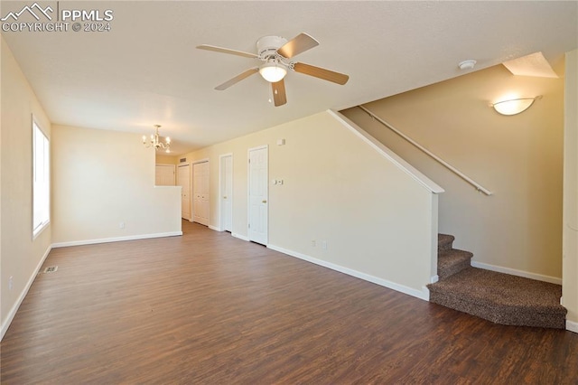 unfurnished living room with ceiling fan with notable chandelier and dark wood-type flooring