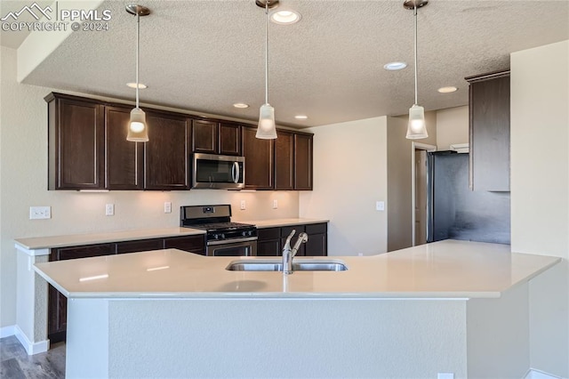 kitchen with pendant lighting, a textured ceiling, wood-type flooring, stainless steel appliances, and sink