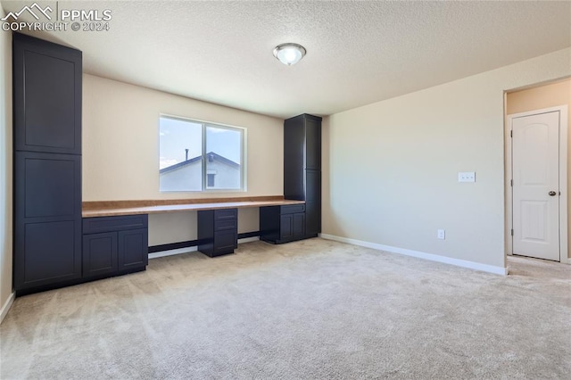 interior space with a textured ceiling, light carpet, and built in desk