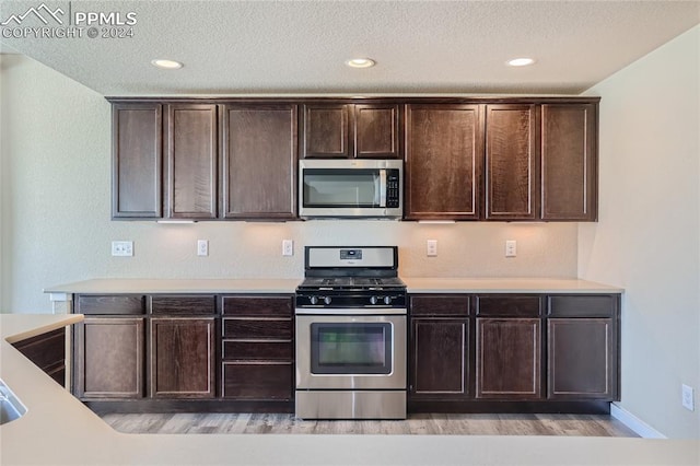 kitchen featuring a textured ceiling, appliances with stainless steel finishes, dark brown cabinets, and light wood-type flooring