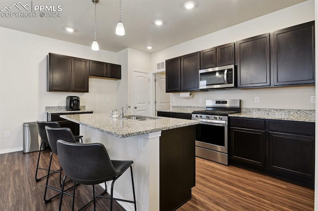 kitchen featuring a kitchen island with sink, dark wood-type flooring, sink, appliances with stainless steel finishes, and a kitchen bar