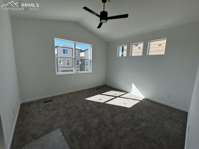 spare room with ceiling fan, vaulted ceiling, and dark colored carpet