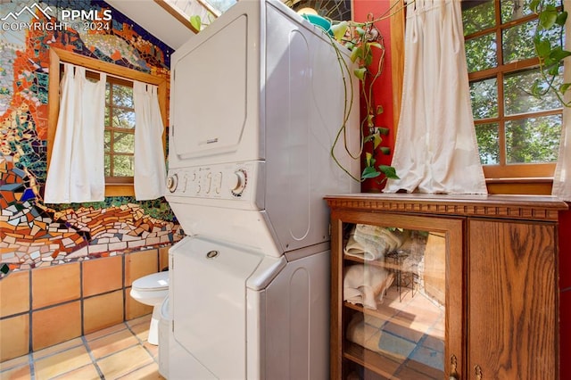 laundry area featuring stacked washer and clothes dryer, a healthy amount of sunlight, and light tile patterned floors