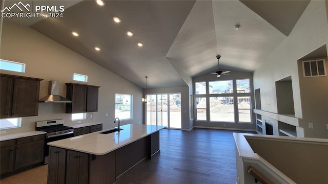 kitchen featuring a kitchen island with sink, wall chimney range hood, stainless steel gas range, light stone countertops, and tasteful backsplash