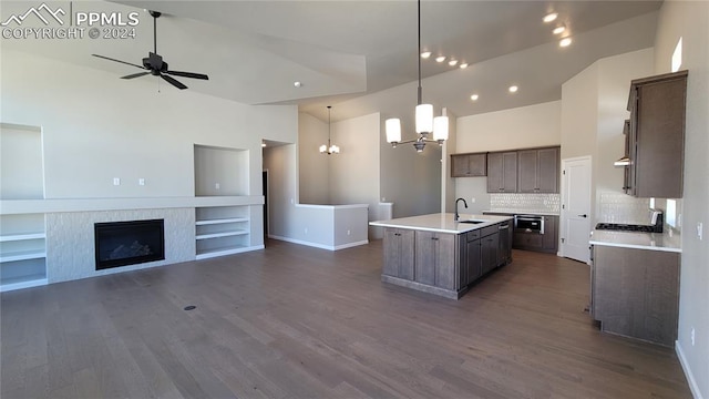 kitchen with backsplash, ceiling fan with notable chandelier, decorative light fixtures, built in features, and an island with sink