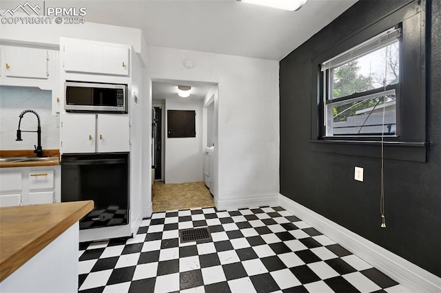 kitchen with tasteful backsplash, white cabinets, sink, stainless steel microwave, and light tile patterned floors