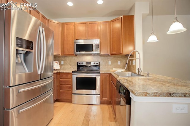 kitchen featuring appliances with stainless steel finishes, decorative backsplash, sink, hanging light fixtures, and light hardwood / wood-style flooring