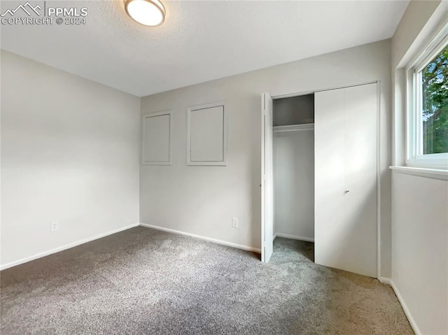 unfurnished bedroom featuring a textured ceiling, carpet floors, a closet, and baseboards