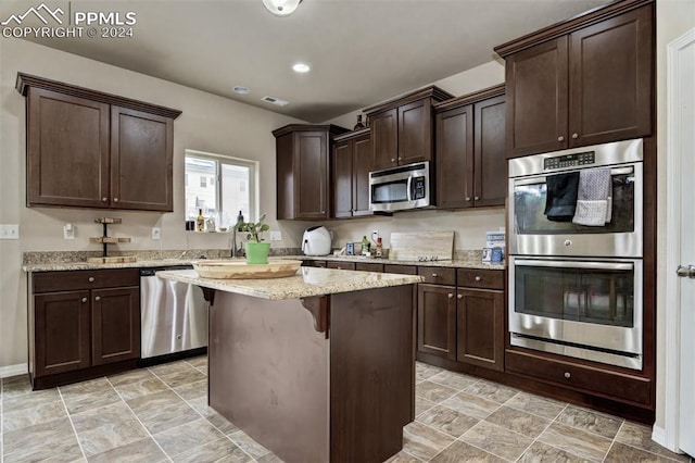 kitchen featuring a breakfast bar, light stone countertops, a kitchen island, dark brown cabinetry, and stainless steel appliances