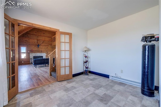 spare room with french doors, vaulted ceiling, a stone fireplace, and wooden walls