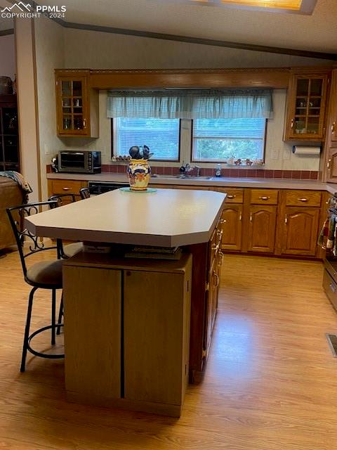 kitchen with a breakfast bar, vaulted ceiling, light hardwood / wood-style flooring, and a kitchen island