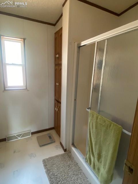 bathroom with a shower with shower door and ornamental molding