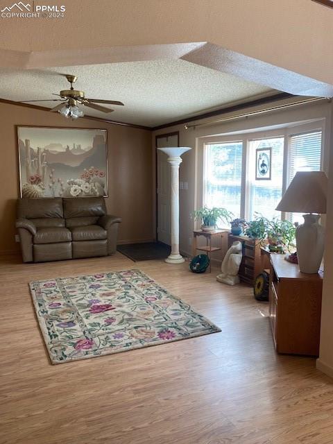 living room featuring crown molding, a textured ceiling, ceiling fan, hardwood / wood-style floors, and ornate columns