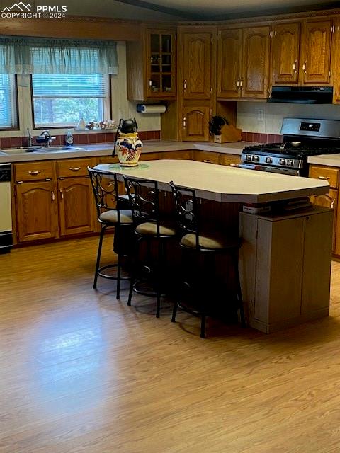 kitchen with gas range, sink, range hood, a breakfast bar area, and light hardwood / wood-style floors