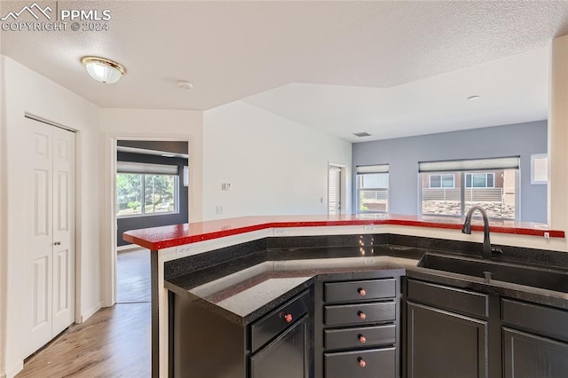 kitchen featuring a textured ceiling, light wood-type flooring, dark stone countertops, and sink