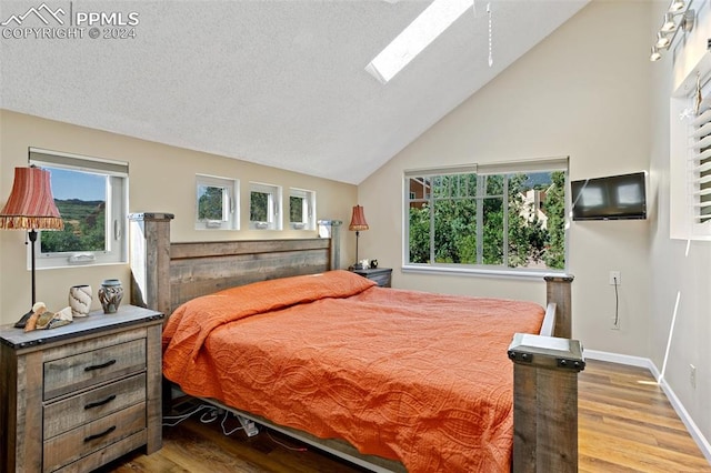 bedroom featuring a textured ceiling, vaulted ceiling with skylight, and wood-type flooring