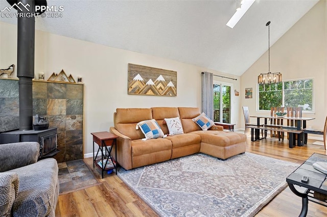 living room featuring a wood stove, a notable chandelier, tile walls, hardwood / wood-style floors, and high vaulted ceiling