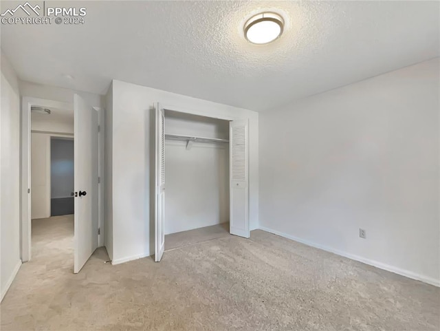 unfurnished bedroom featuring light colored carpet, a textured ceiling, and a closet