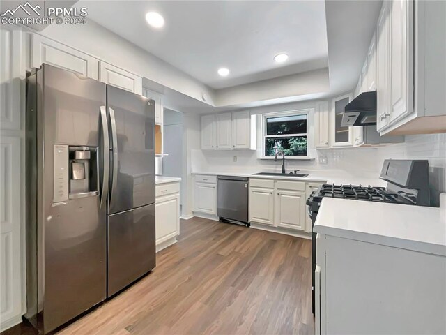 kitchen featuring appliances with stainless steel finishes, wall chimney exhaust hood, sink, hardwood / wood-style flooring, and white cabinetry