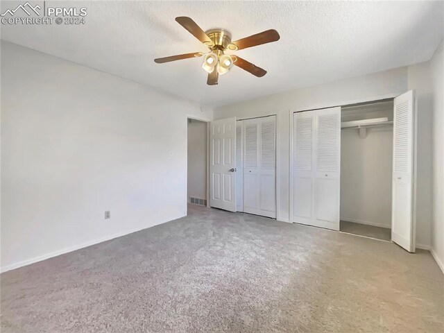 unfurnished bedroom featuring carpet, a textured ceiling, two closets, and ceiling fan