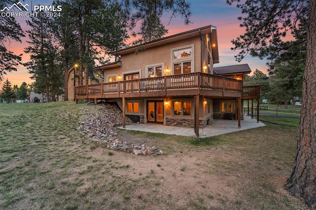 back house at dusk with a deck, a yard, and a patio