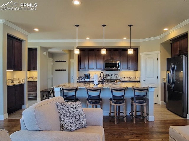 kitchen with an island with sink, black refrigerator with ice dispenser, and hanging light fixtures