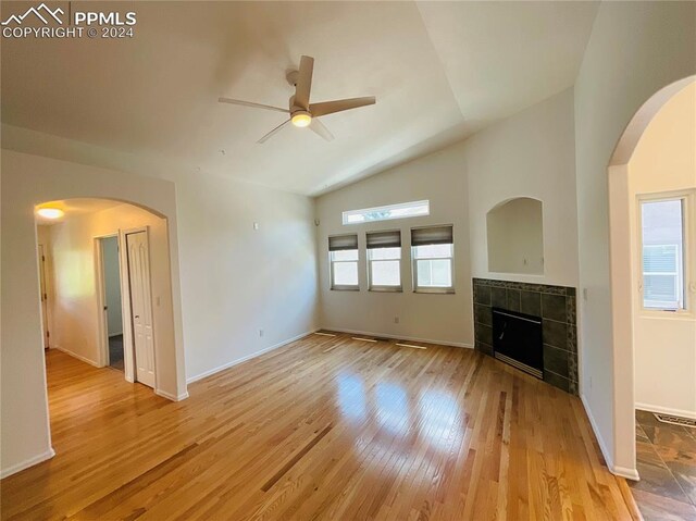 unfurnished living room featuring vaulted ceiling, light hardwood / wood-style flooring, a tile fireplace, and ceiling fan