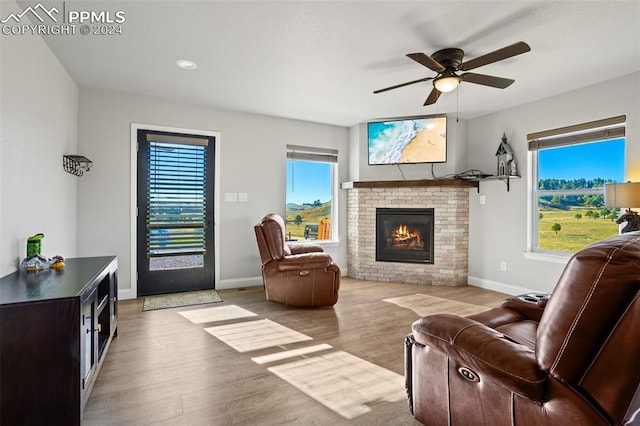 living room with a brick fireplace, light hardwood / wood-style flooring, and ceiling fan