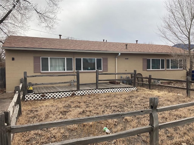 ranch-style house featuring roof with shingles, concrete block siding, fence, and a wooden deck