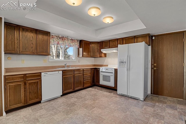 kitchen featuring decorative backsplash, white appliances, a tray ceiling, and sink