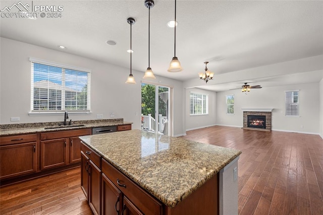 kitchen with a center island, sink, hanging light fixtures, light stone countertops, and ceiling fan with notable chandelier