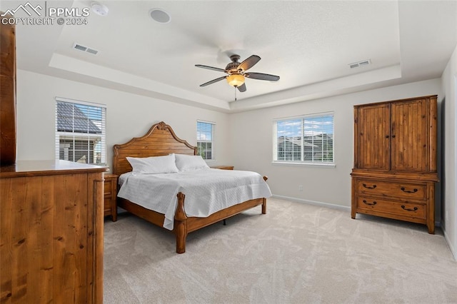 bedroom featuring light carpet, ceiling fan, and a raised ceiling