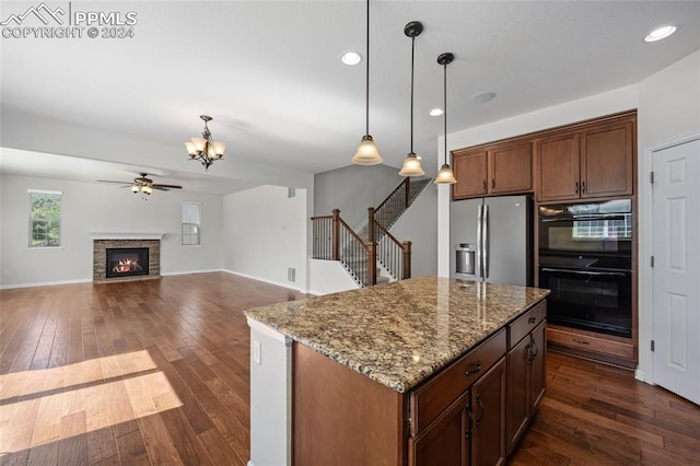 kitchen featuring light stone countertops, decorative light fixtures, double oven, a stone fireplace, and stainless steel fridge