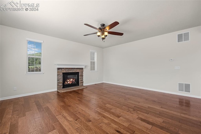 unfurnished living room with ceiling fan, a stone fireplace, and hardwood / wood-style flooring