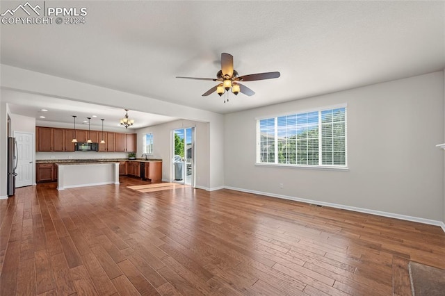 unfurnished living room featuring a healthy amount of sunlight, dark wood-type flooring, and ceiling fan with notable chandelier